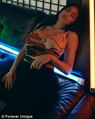 Η Kylie Jenner ποζάρει σε δερμάτινο καναπέ με αμάνικη μπλούζα παραλλαγής και φωτισμό νέον.