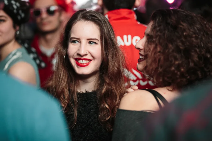 Νεαρή γυναίκα με κόκκινο κραγιόν χαμογελά σε πάρτι.