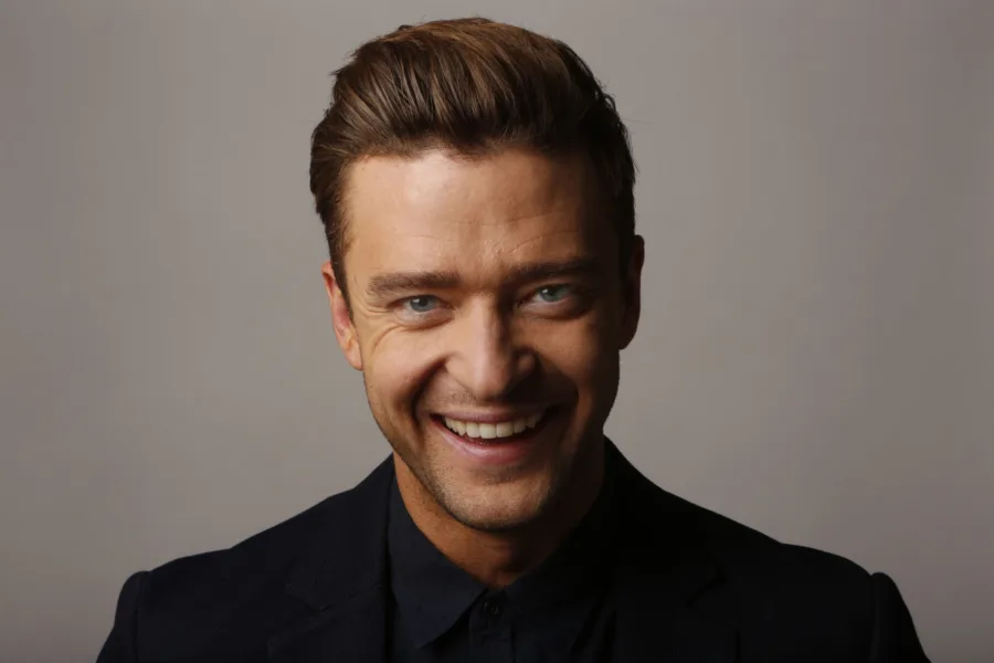 Ο Justin Timberlake χαμογελάει φορώντας μαύρο πουκάμισο και σακάκι.