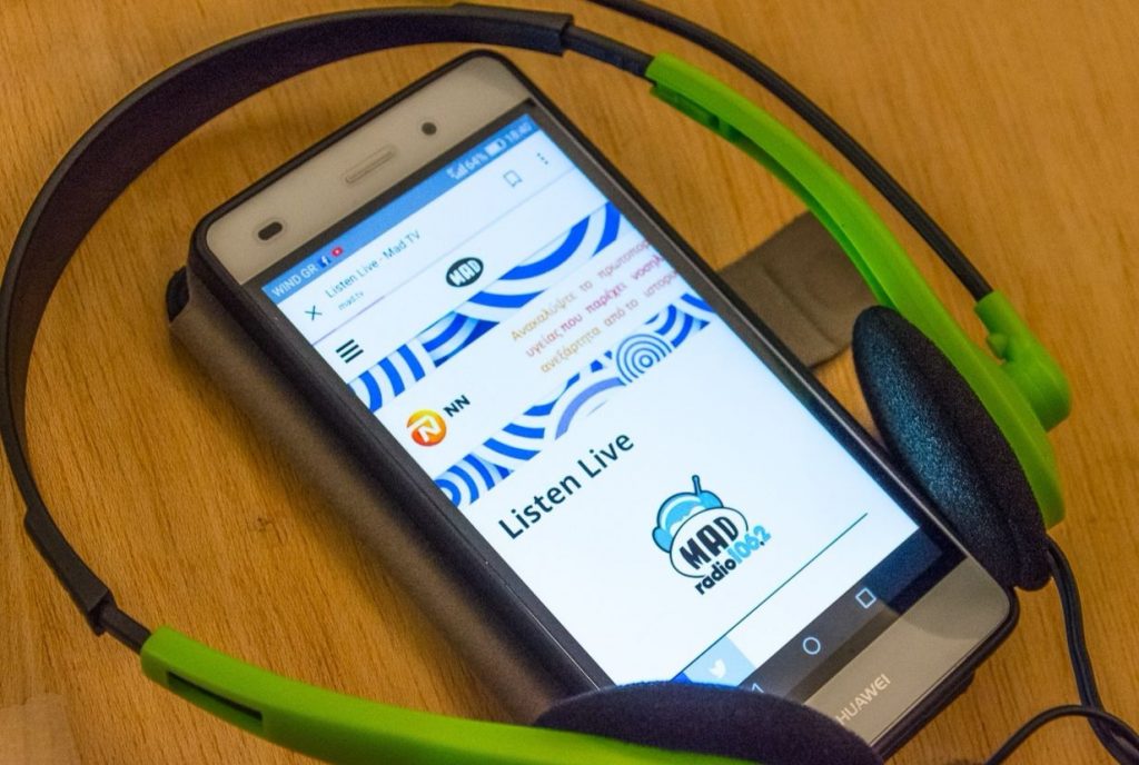 Smartphone με την ιστοσελίδα του Mad TV και ακουστικά κεφαλής.