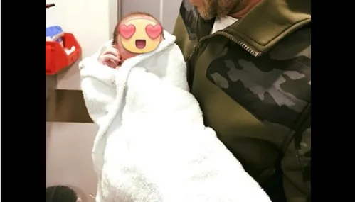 Ένας άνδρας κρατά στην αγκαλιά του ένα νεογέννητο μωρό τυλιγμένο σε λευκή πετσέτα.