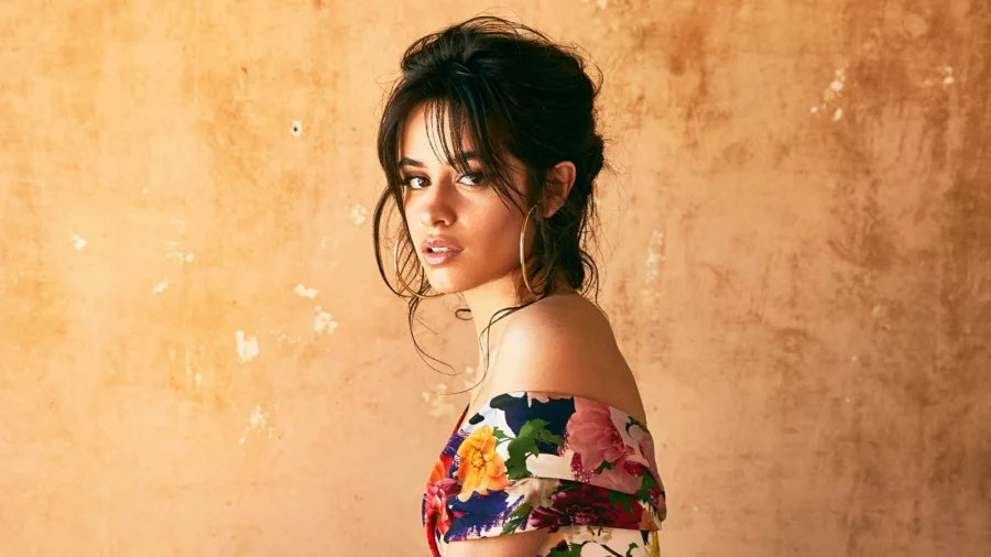 Η Camila Cabello ποζάρει με φλοράλ ρούχο σε φόντο με υφή ώχρας.