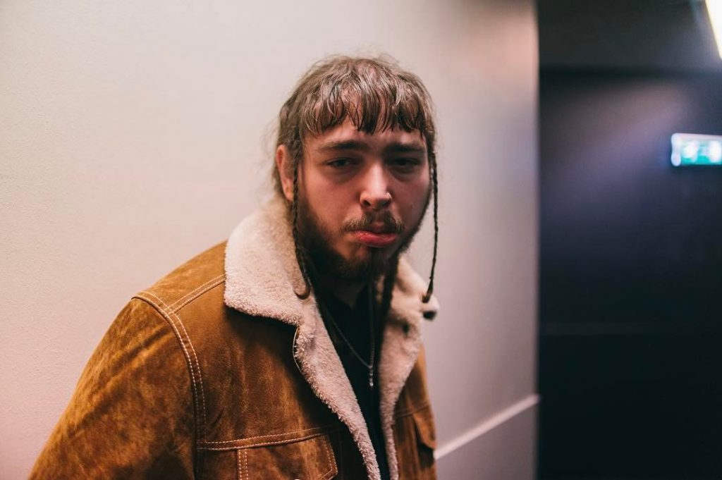 Ο Post Malone με καφέ σουέντ τζάκετ και γούνα, κοιτάζοντας την κάμερα.