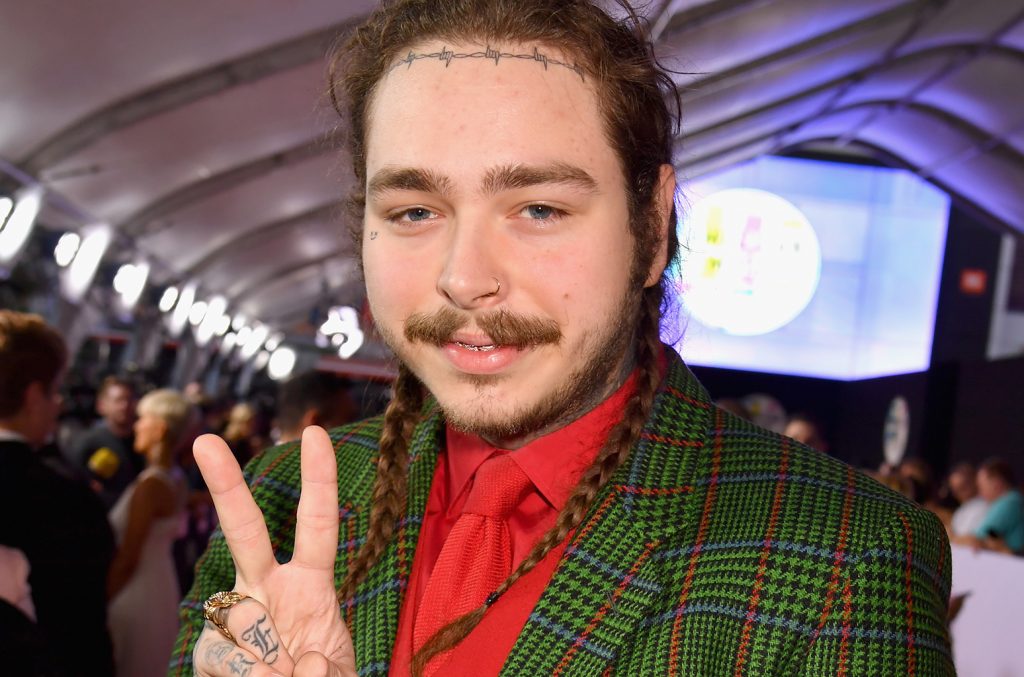 Ο Post Malone με πράσινο καρό σακάκι και κόκκινο πουκάμισο κάνει το σήμα της ειρήνης.