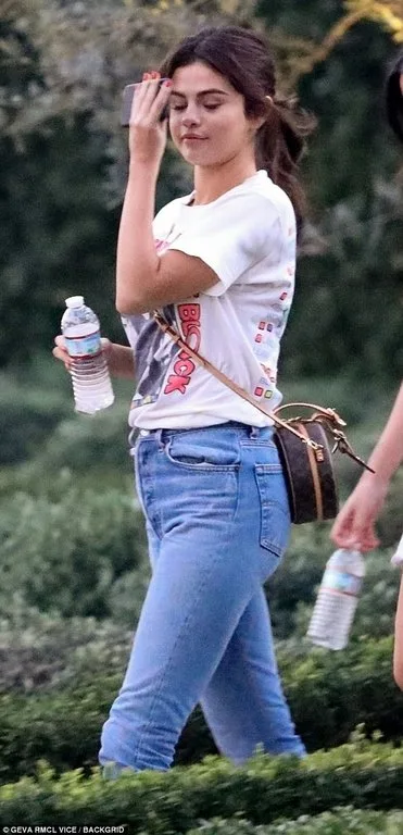 Η Selena Gomez περπατάει σε εξωτερικό χώρο κρατώντας ένα μπουκάλι νερό.
