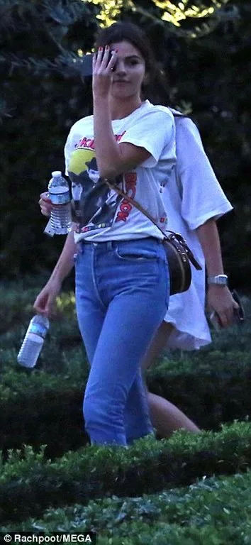 Η Selena Gomez περπατάει σε εξωτερικό χώρο κρατώντας μπουκάλια νερό.