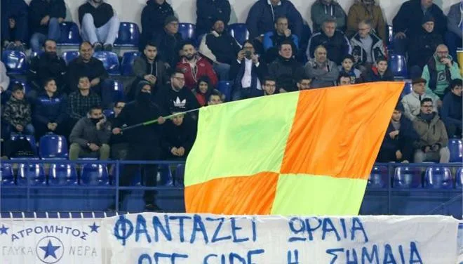 Οπαδός στις κερκίδες κρατάει μια μεγάλη κίτρινη και πορτοκαλί σημαία οφσάιντ.