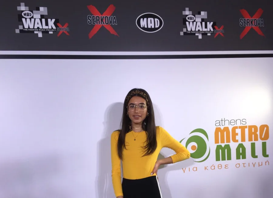 Μια νεαρή κοπέλα ποζάρει μπροστά από το backdrop του MadWalk 2018 by Serkova στο Athens Metro Mall.