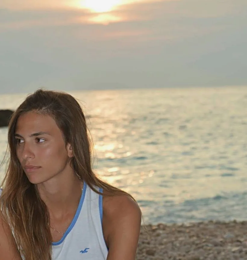 Η σύντροφος του Γιάννη Δρυμωνάκου σε παραλία κατά τη διάρκεια του ηλιοβασιλέματος.
