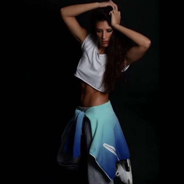Γυναίκα με αθλητικό στυλ, λευκό crop top και γαλάζια ζακέτα δεμένη στη μέση.