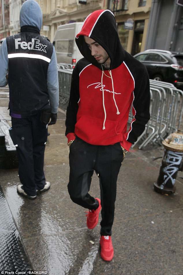 Ο Zayn Malik περπατά στο δρόμο φορώντας κόκκινο και μαύρο φούτερ.