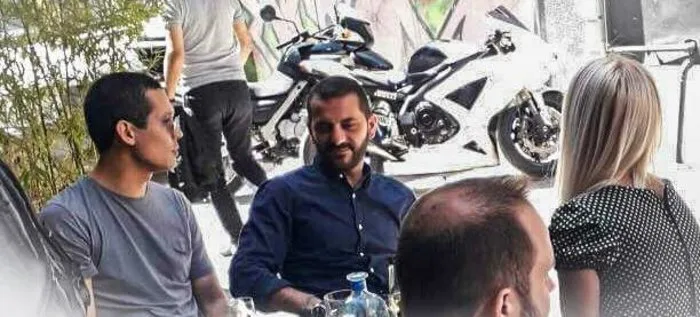 Παίκτες και κριτές του MasterChef σε τραπέζι με φόντο μια μοτοσυκλέτα.