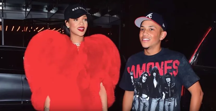 Η Rihanna με κόκκινο γούνινο παλτό σε σχήμα καρδιάς δίπλα σε έναν άνδρα.