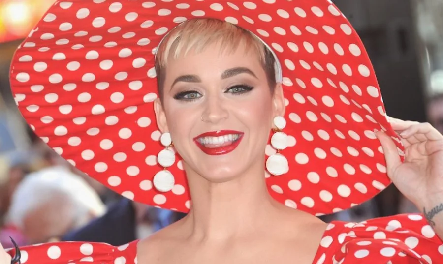 Η Katy Perry με ξανθά κοντά μαλλιά, κόκκινο πουά καπέλο και ασορτί φόρεμα.
