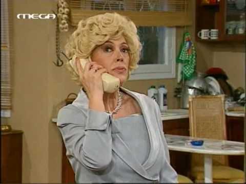Γυναίκα με ξανθά σγουρά μαλλιά μιλάει στο τηλέφωνο σε σκηνή από ελληνική σειρά.