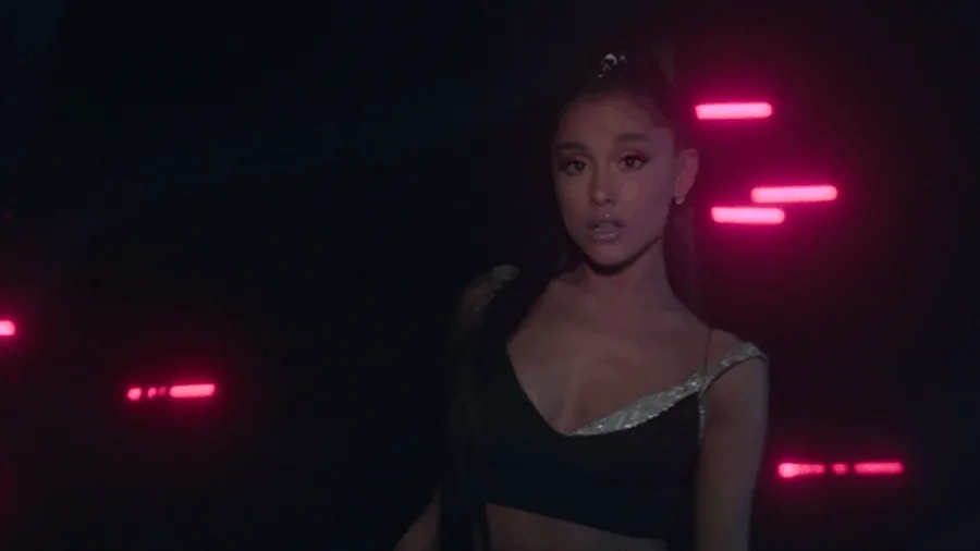 Η Ariana Grande σε σκοτεινό σκηνικό με ροζ φώτα νέον.