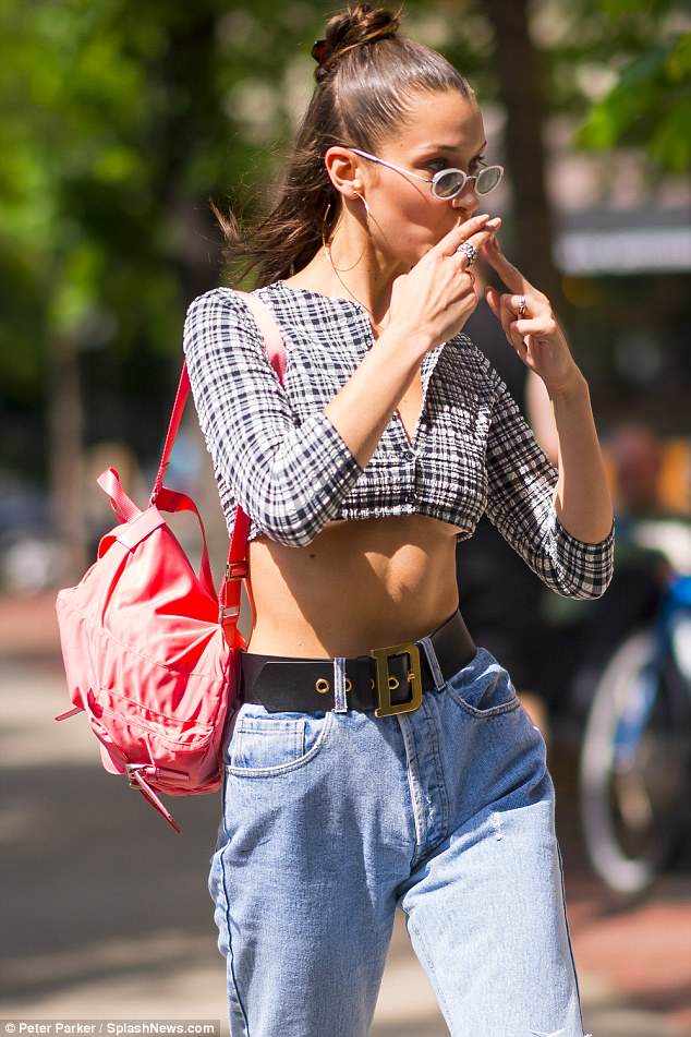Η Bella Hadid με καρό crop top, τζιν παντελόνι και ροζ σακίδιο πλάτης περπατά στο δρόμο.