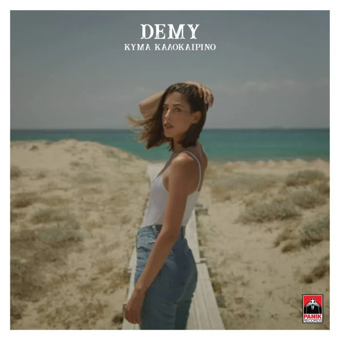Η Demy σε παραλία με λευκό φανελάκι και τζιν παντελόνι.