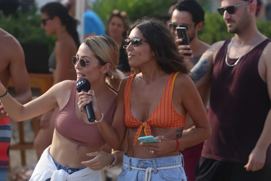 Δύο γυναίκες σε εκδήλωση beach volley, η μία κρατάει μικρόφωνο του MAD.