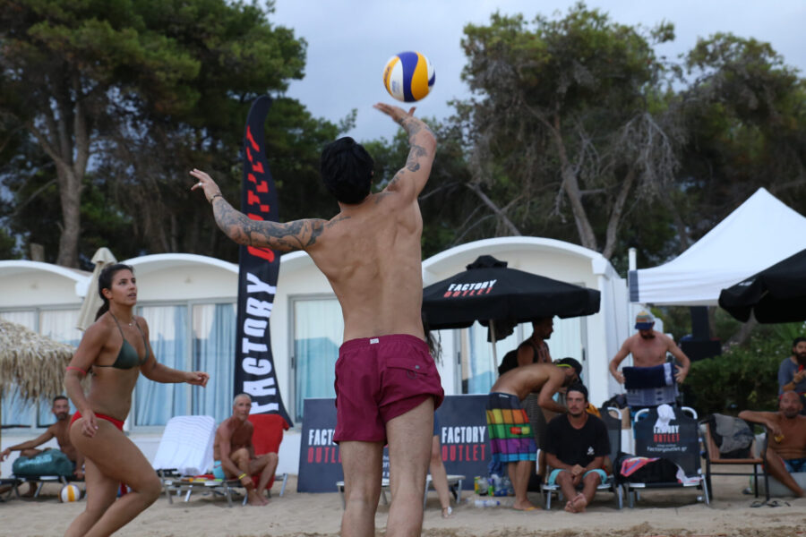 Άνδρας και γυναίκα παίζουν beach volley σε παραλία.