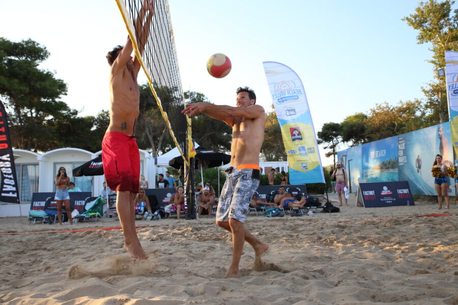 Δύο άνδρες παίζουν beach volley σε παραλία.