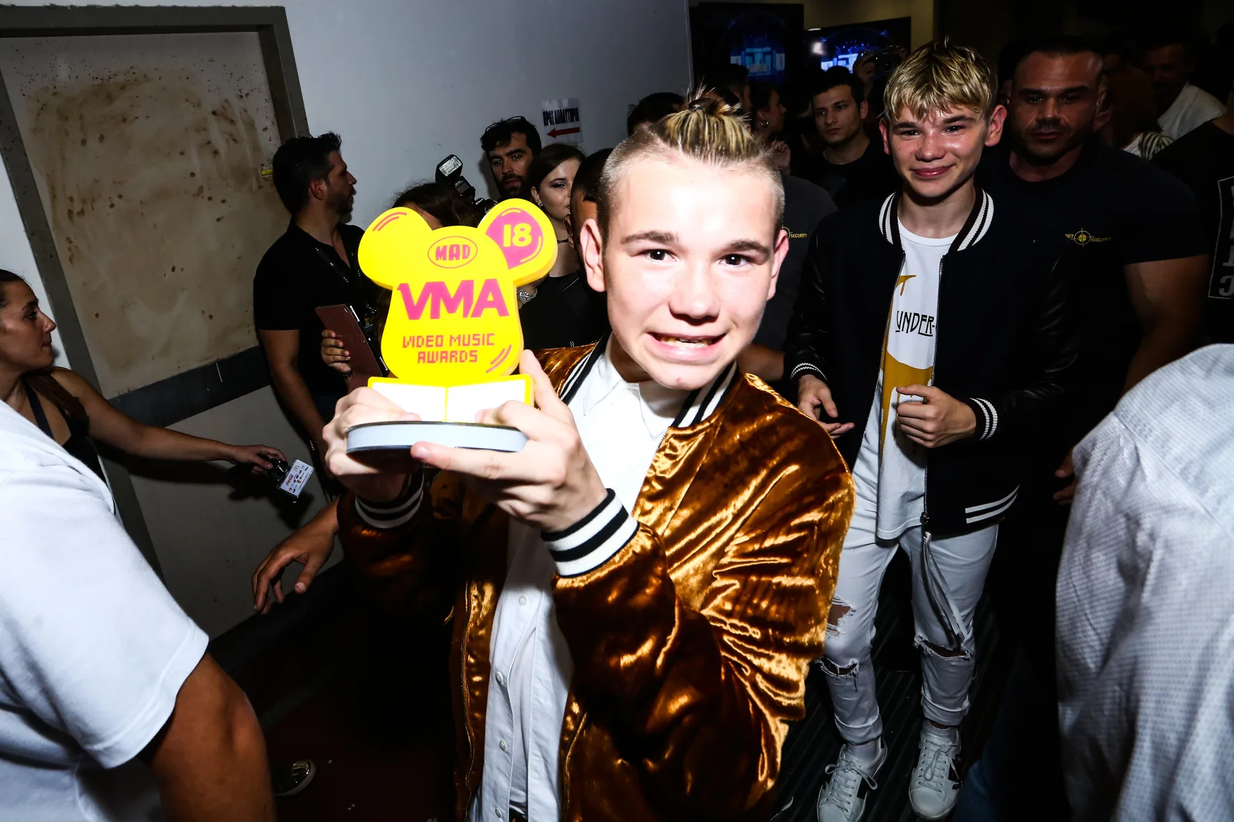 Δύο νεαροί καλλιτέχνες στα backstage των Mad Video Music Awards 2018, με τον έναν να κρατάει το κίτρινο βραβείο της διοργάνωσης.