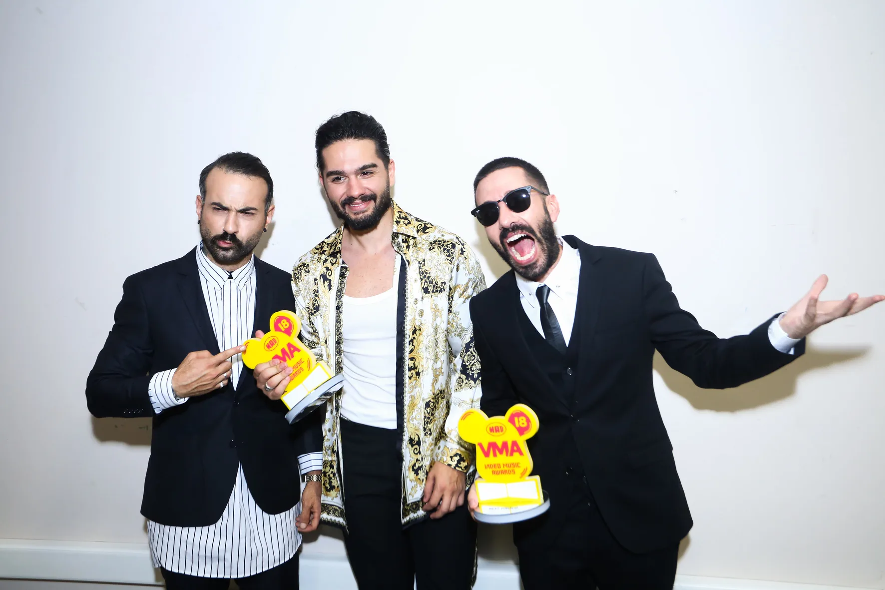Τρεις άνδρες καλλιτέχνες ποζάρουν στα backstage των Mad Video Music Awards 2018 κρατώντας βραβεία.