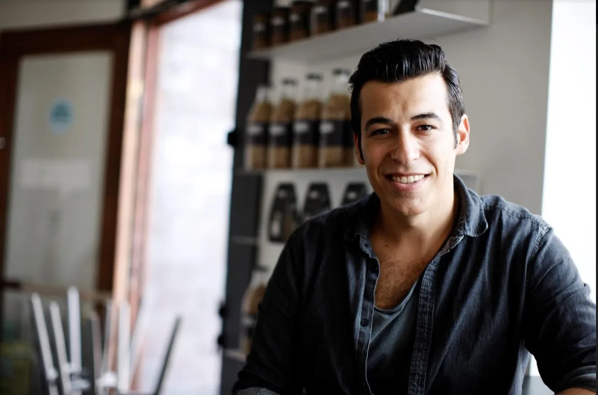Ο Άκης Πετρετζίκης χαμογελάει σε εσωτερικό χώρο.