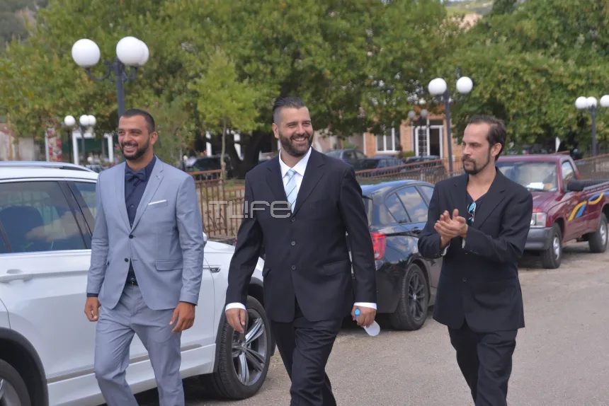 Ο Βαγγέλης Σερίφης με κοστούμι περπατάει σε εξωτερικό χώρο.