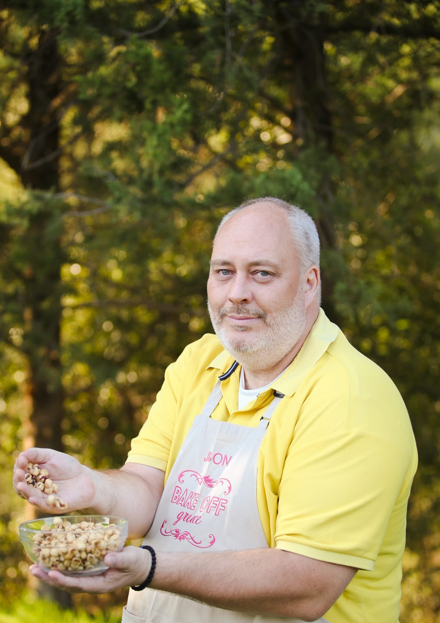 Ο Ιάσονας, παίκτης του Bake Off Greece, κρατάει ένα μπολ με φουντούκια σε εξωτερικό χώρο.