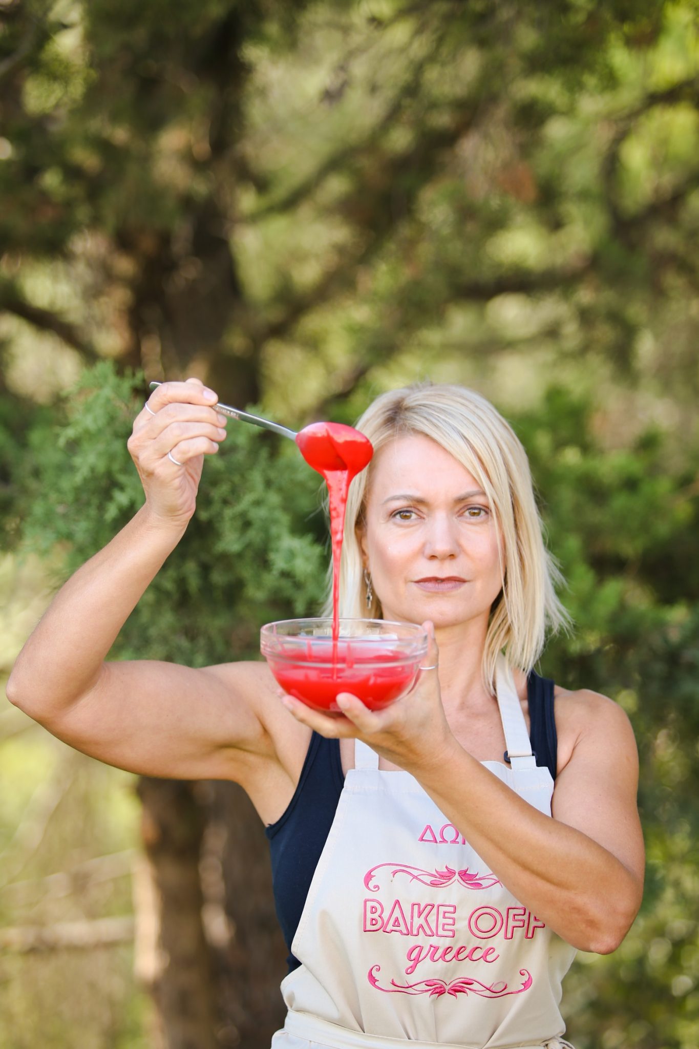 Παίκτρια του Bake Off Greece κρατάει μπολ και κουτάλι με κόκκινο γλάσο.
