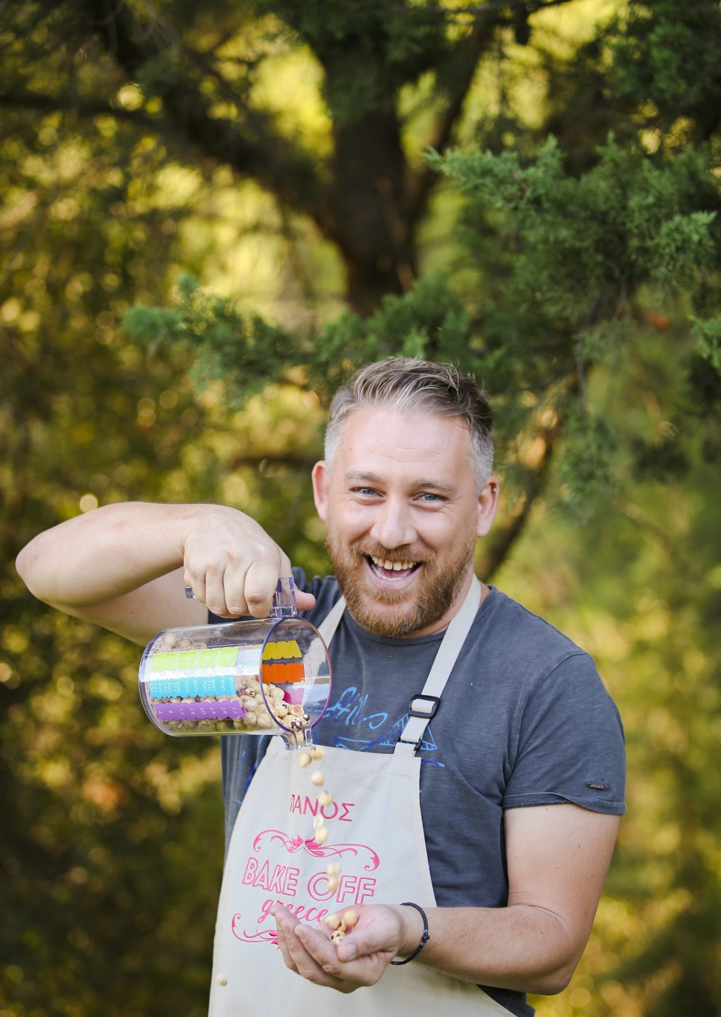 Ο Πάνος από το Bake Off Greece ρίχνει ξηρούς καρπούς από δοσομετρητή στο χέρι του.