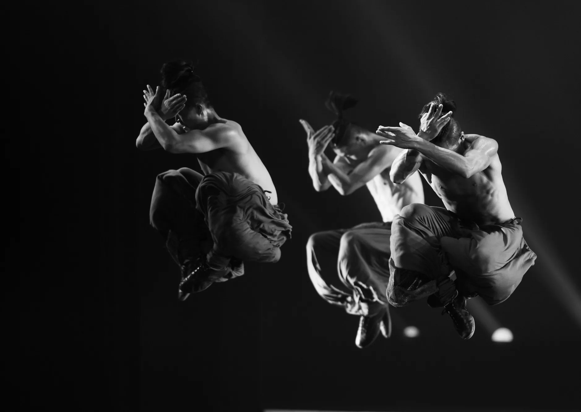 Τρεις άνδρες χορευτές των Kung Fu Warriors σε άλμα κατά τη διάρκεια παράστασης.
