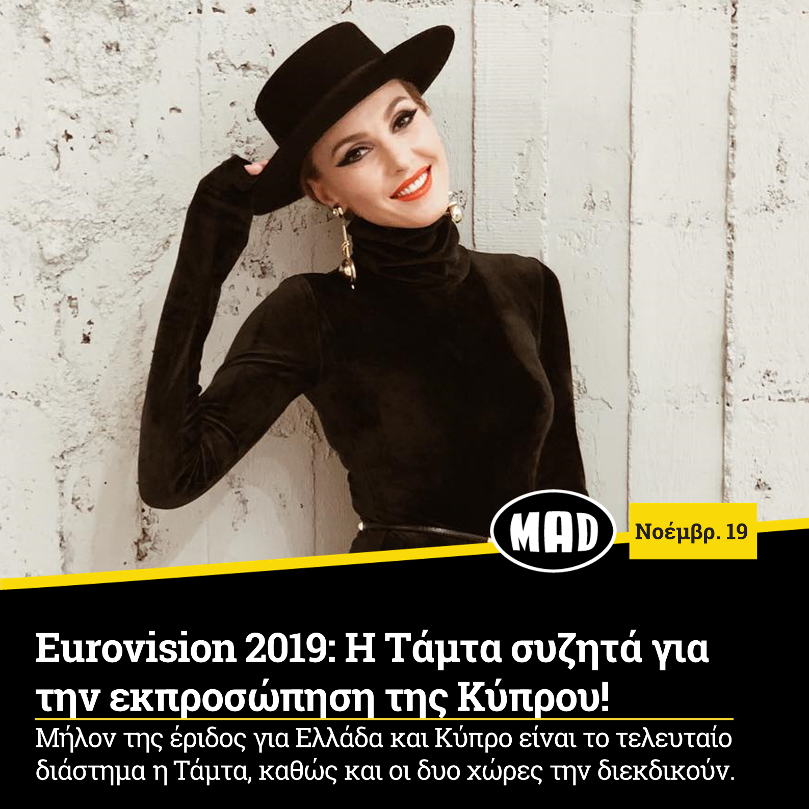 Η Τάμτα με μαύρο καπέλο και ζιβάγκο ποζάρει μπροστά από λευκό τοίχο.