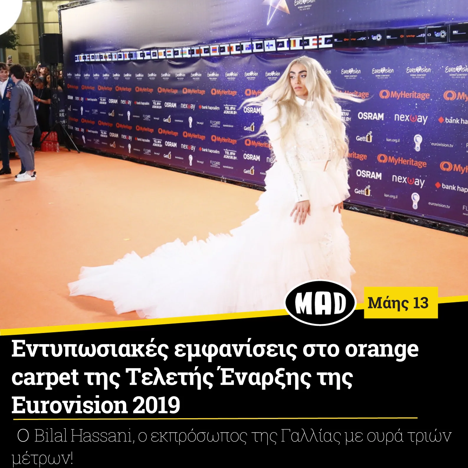 Καλλιτέχνης με μακρύ λευκό φόρεμα στο πορτοκαλί χαλί της Eurovision 2019.