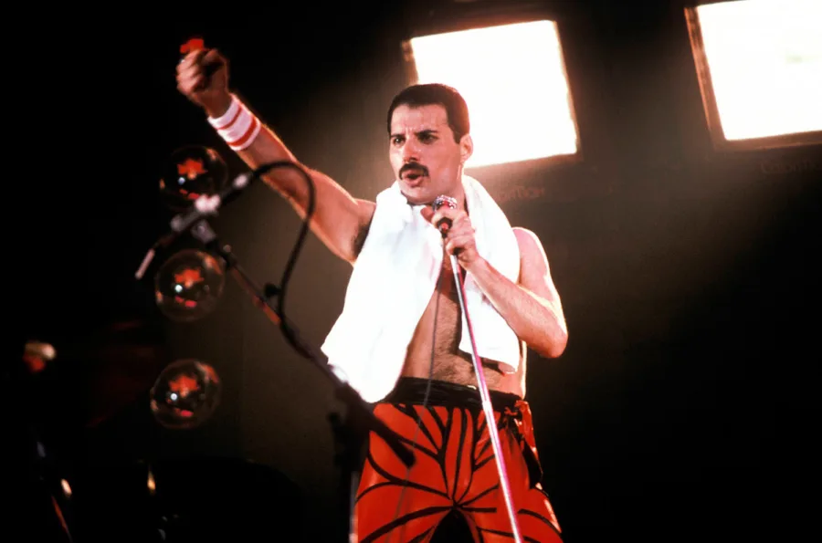 Ο Freddie Mercury σε συναυλία με υψωμένη γροθιά και πετσέτα στους ώμους.
