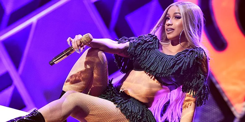 Η Cardi B στη σκηνή με μαύρο σύνολο με κρόσσια και χρυσό μικρόφωνο.