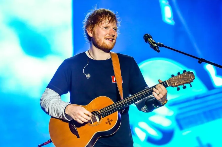 Ο Ed Sheeran παίζει κιθάρα και τραγουδάει σε συναυλία.