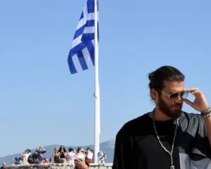 Ο Can Yaman με γυαλιά ηλίου μπροστά από την ελληνική σημαία.
