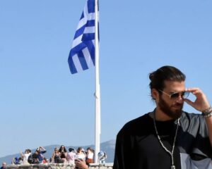 Ο Can Yaman με γυαλιά ηλίου μπροστά από την ελληνική σημαία.
