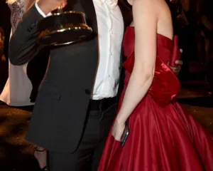Ένας άνδρας με κοστούμι κρατά ένα βραβείο Emmy και αγκαλιάζει μια γυναίκα με κόκκινο φόρεμα.