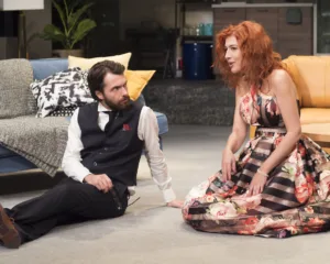 Σκηνή από την παράσταση «Όποιος θέλει να χωρίσει…να σηκώσει το χέρι του!» με δύο ηθοποιούς στο πάτωμα.