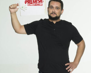 Ο κωμικός Πάρης Ρούπος κρατάει μια πινακίδα Premise Comedy Club.