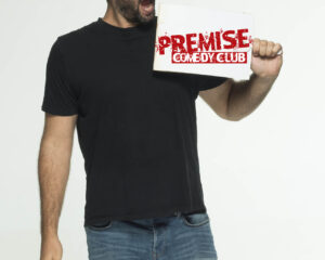 Ο Γιώργος Χατζηπαύλου κρατάει πινακίδα του Premise Comedy Club.