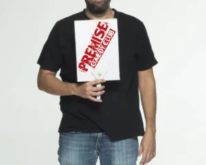 Ο Λάμπρος Φισφής κρατάει πινακίδα του Premise Comedy Club.