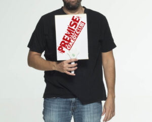 Ο Λάμπρος Φισφής κρατάει πινακίδα του Premise Comedy Club.
