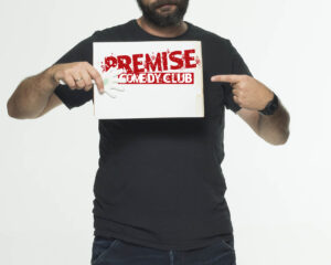 Ο Γιώργος Χατζηπαύλου κρατάει μια πινακίδα Premise Comedy Club.