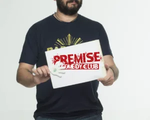 Ο Πάρης Ρούπος κρατάει μια πινακίδα Premise Comedy Club.