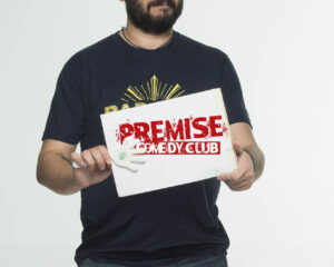 Ο Πάρης Ρούπος κρατάει μια πινακίδα Premise Comedy Club.