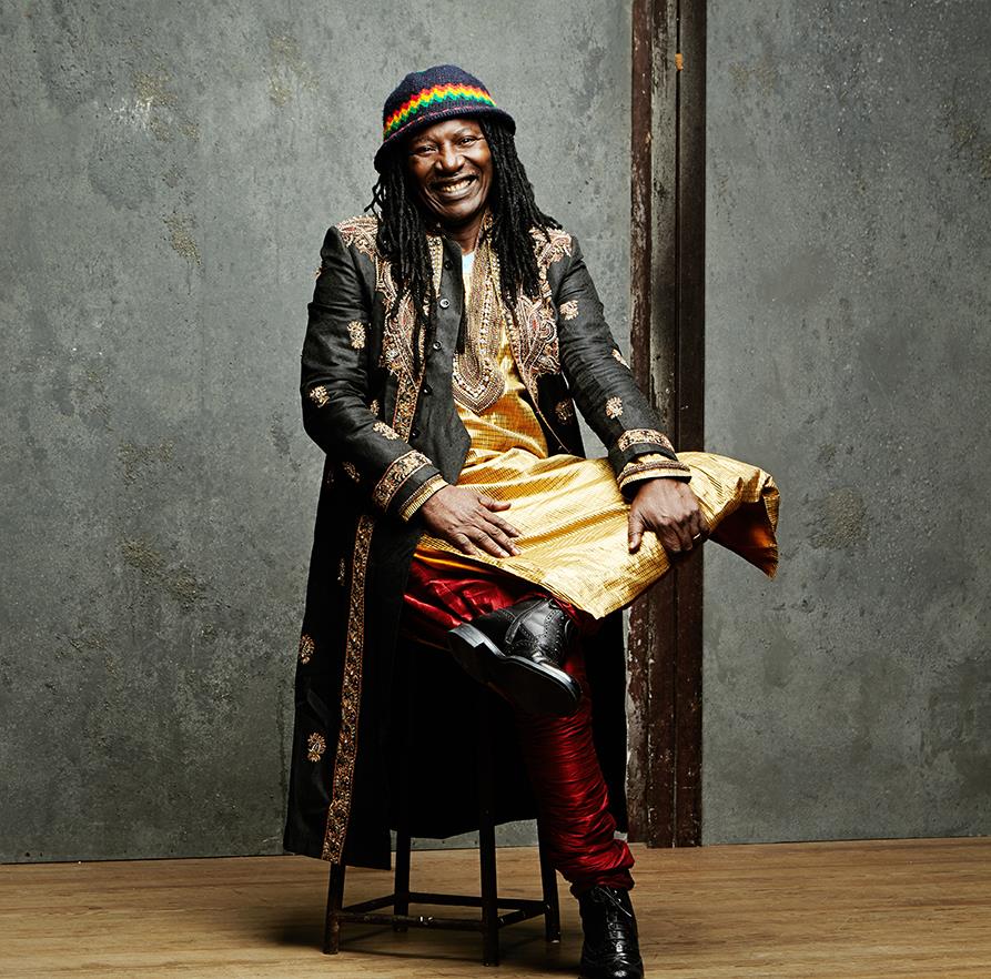Ο Alpha Blondy κάθεται σε σκαμπό.